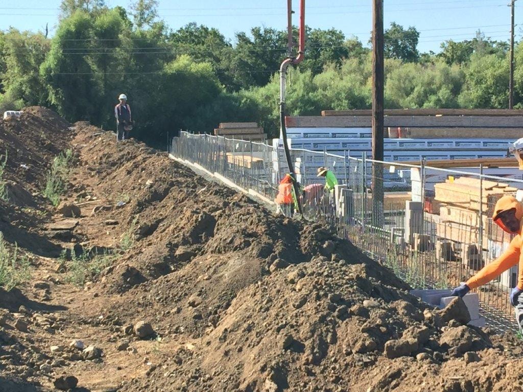 Workers setting masonry block along excavated foundation